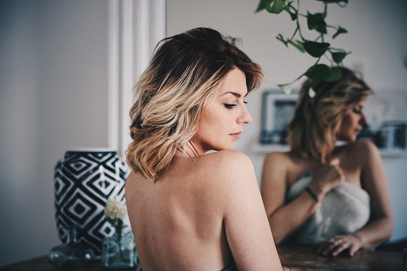 eine Frau mit blonden Haaren, die ihren Körper mit einem Handtuch vor dem Spiegel bedeckt