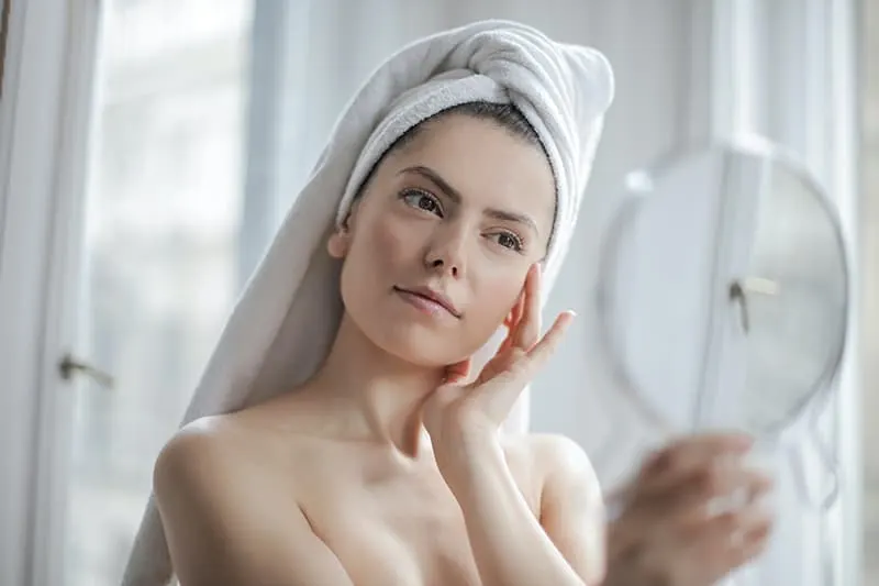 eine Frau mit einem Handtuch auf dem Kopf, die sich in den Spiegel schaut
