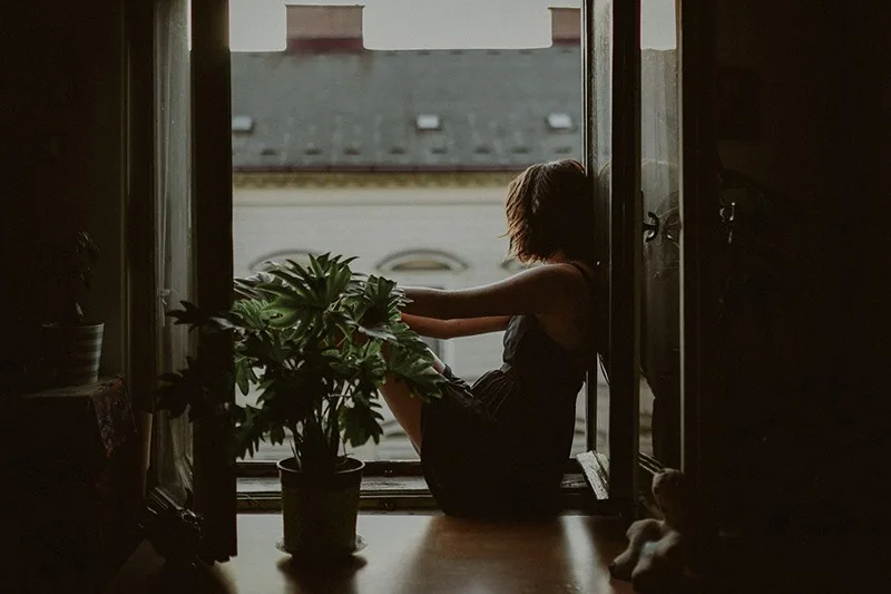 eine Frau, die auf dem Fensterbrett sitzt und nach draußen schaut