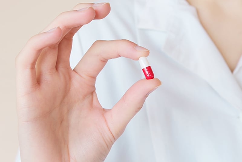 eine Krankenschwester demonstriert eine kleine Pille, die sie mit den Fingern hält