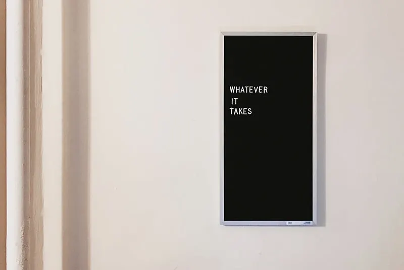 eine Tafel mit dem Text "Was auch immer es braucht" in englischer Sprache an der Wand