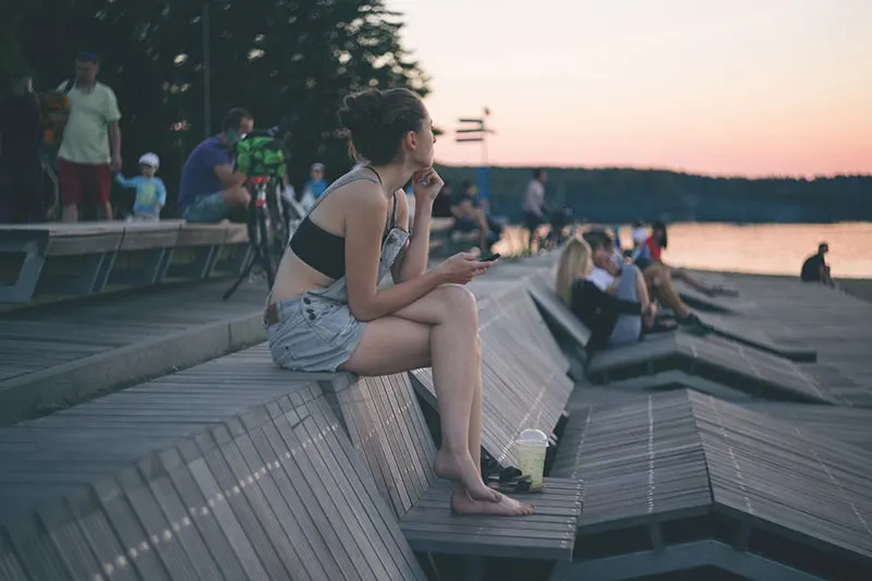 eine barfüßige Frau, die auf der Holzbank sitzt und den Sonnenuntergang beobachtet