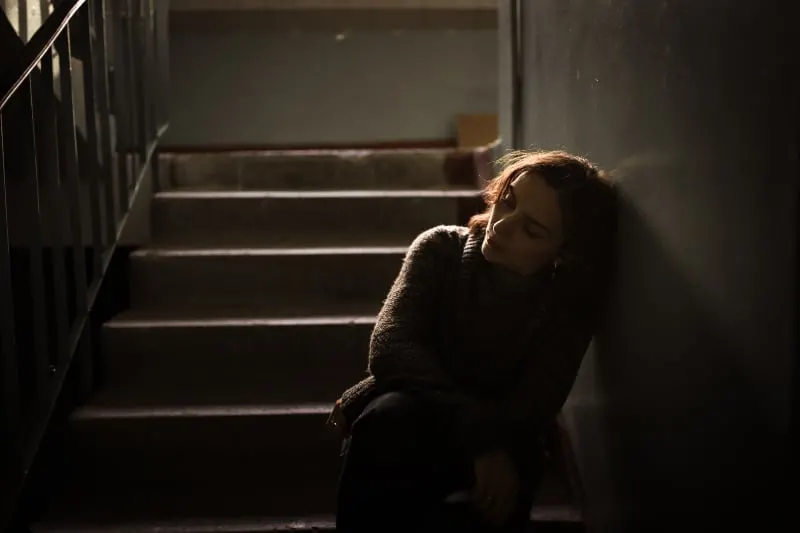 eine depressive Frau, die auf der dunklen Treppe sitzt