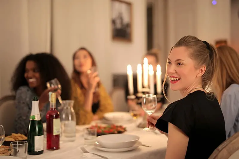eine lächelnde Frau, die mit Freunden während des Abendessens am Tisch sitzt