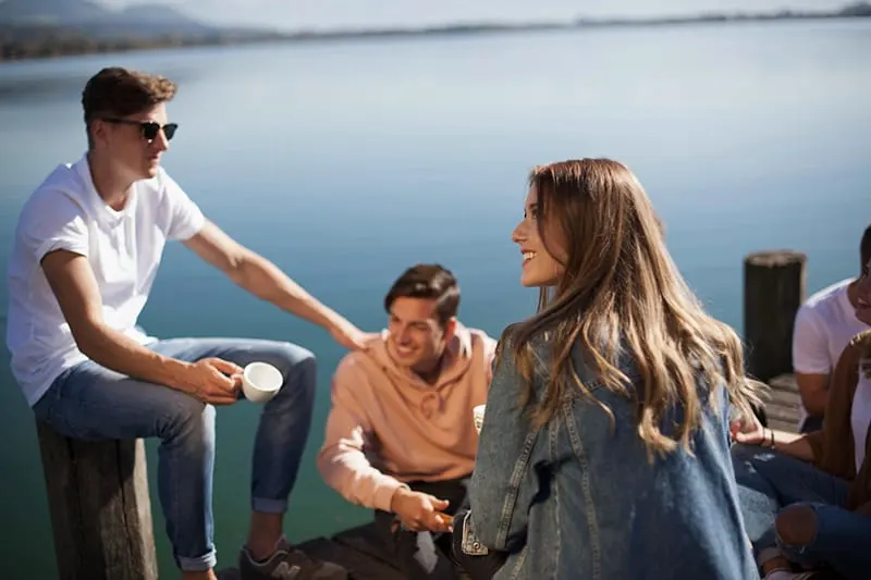 eine lächelnde Frau, die mit Freunden auf einem Bootssteg sitzt