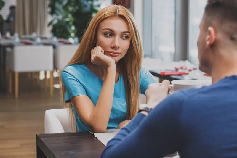eine nachdenkliche Frau, die mit ihrem Freund im Restaurant sitzt und zur Seite schaut