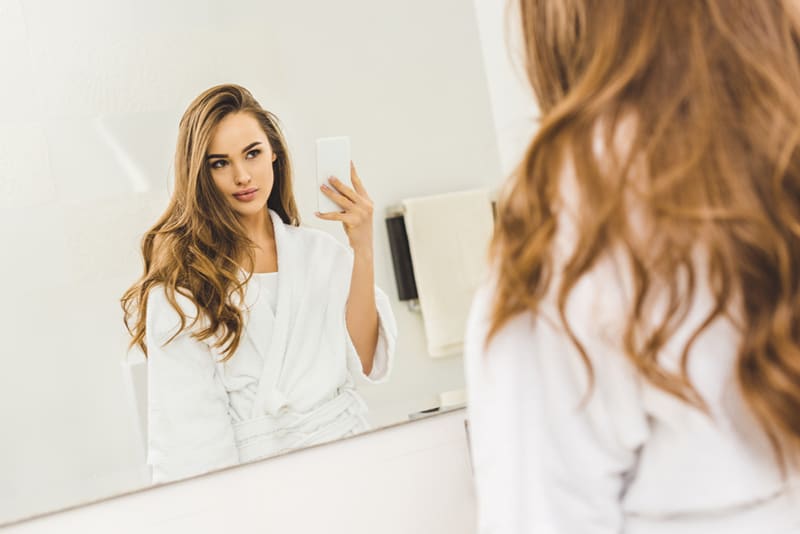 eine selbstbewusste Frau, die Selfie auf Smartphone im Badezimmer nimmt