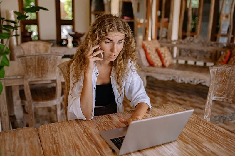 eine stressige Frau, die digitale Geräte benutzt, während sie am Tisch sitzt