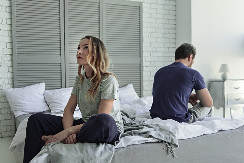 Eine traurige Frau sitzt auf dem Bett und schaut auf, während ihr Mann auf der anderen Seite des Bettes sitzt
