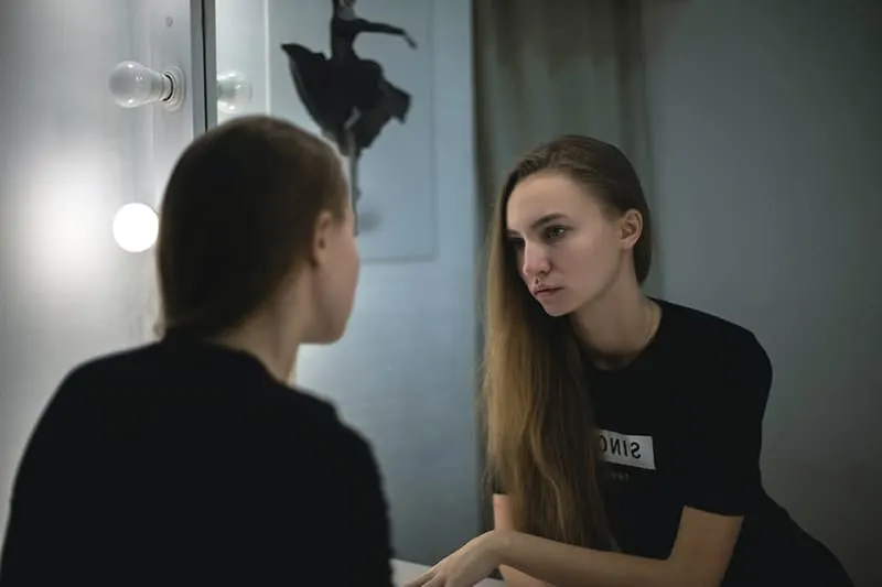 eine traurige Frau, die sich im Spiegel betrachtet, während sie im Raum steht