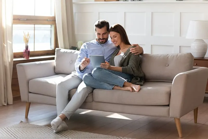 junges Paar sitzt auf der Couch und schaut am digitalen Computer zu