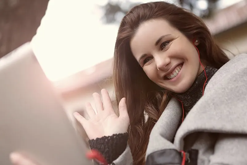 lächelnde Frau winkt während eines Videoanrufs mit ihrem Freund