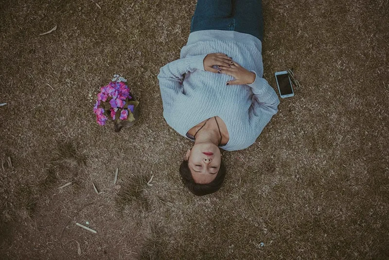 traurige Frau, die auf dem Boden mit Blumen und Handy liegt