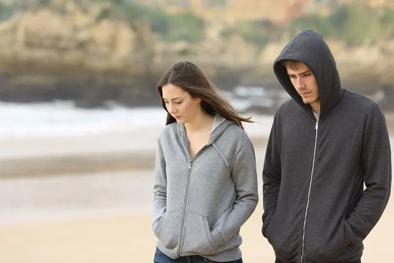 trauriges junges Paar, das auf dem Strand geht