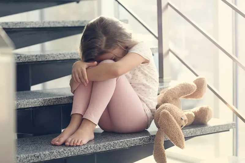 trauriges kleines Mädchen, das auf der Treppe sitzt