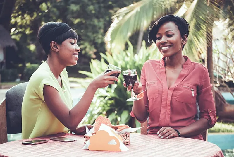 zwei lächelnde Freundinnen, die mit einem Glas Wein anstoßen, während sie in einem Straßencafé sitzen