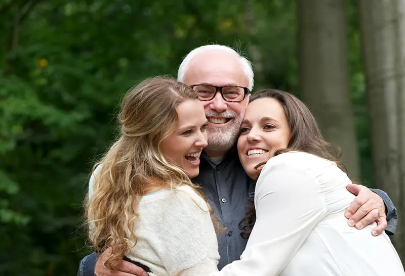 zwei lächelnde Töchter umarmen ihren Vater, während sie im Garten stehen
