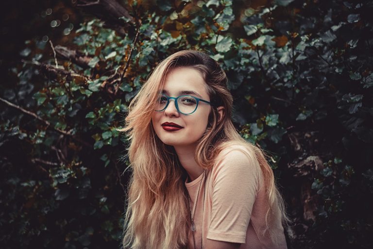 eine Frau mit roten Lippen, die nahe den grünen Pflanzen steht