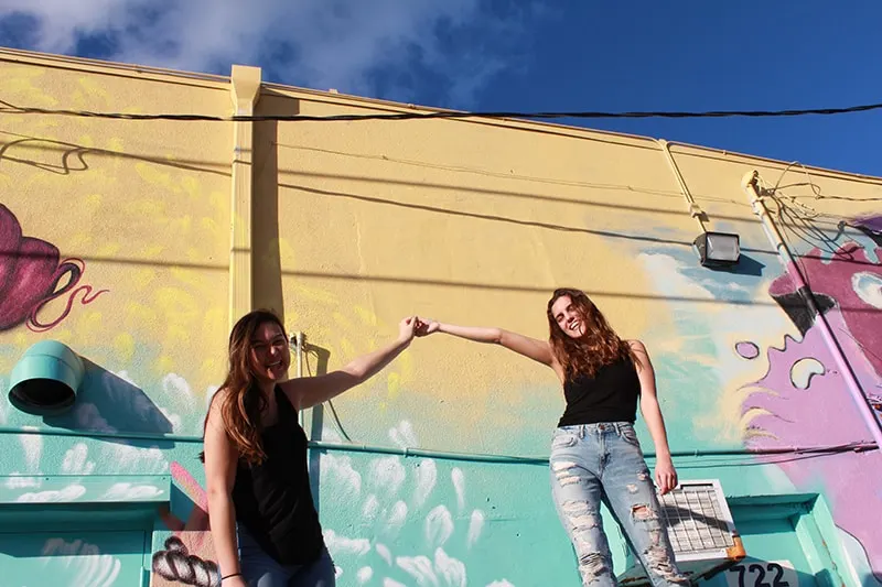 zwei Freundinnen, die Hände halten, während sie nahe der Graffitiwand stehen