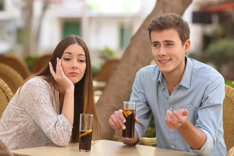 Eine gelangweilte Frau sitzt neben einem Mann und spricht mit ihr über ein Date