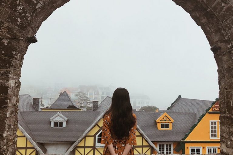 Eine Frau in einem bunten Kleid steht auf einer Steinmauer und beobachtet die Stadt