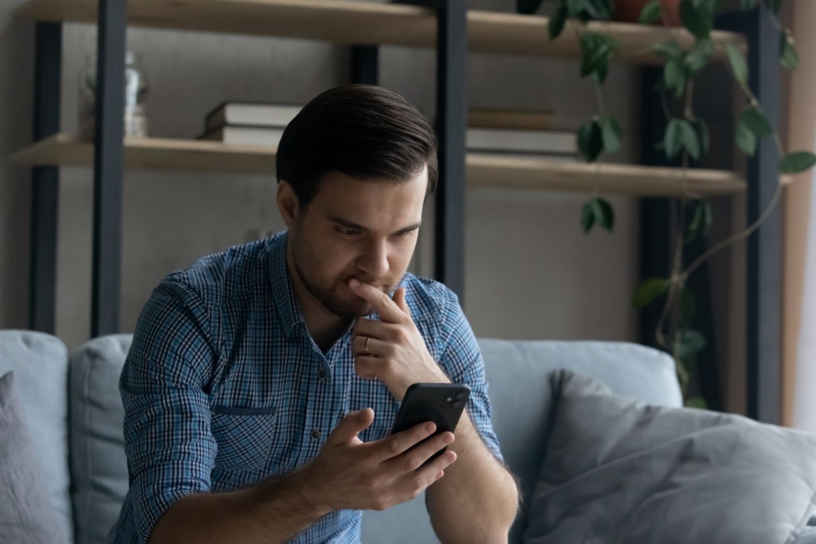 Mann sitzt auf der Couch und schreibt eine SMS