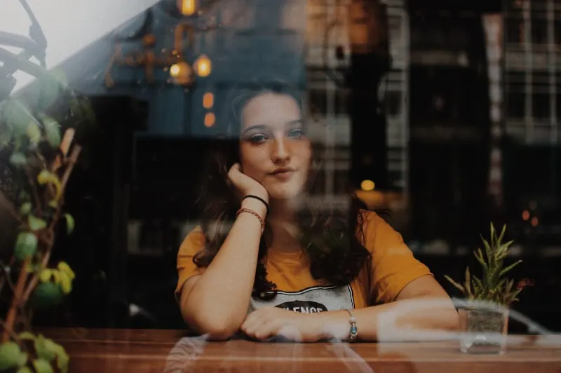 ein Mädchen, das alleine am Caféfenster sitzt