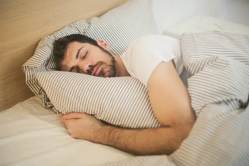 Ein Mann, der fest in einem Bett schläft und ein Bett umarmt