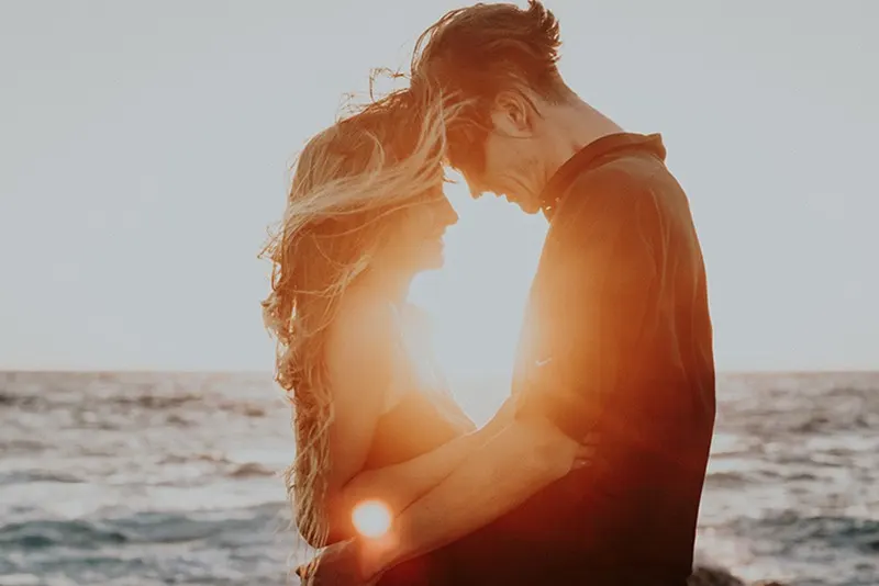 Ein Mann und eine Frau umarmen sich in der Nähe des Meeres während des Sonnenuntergangs