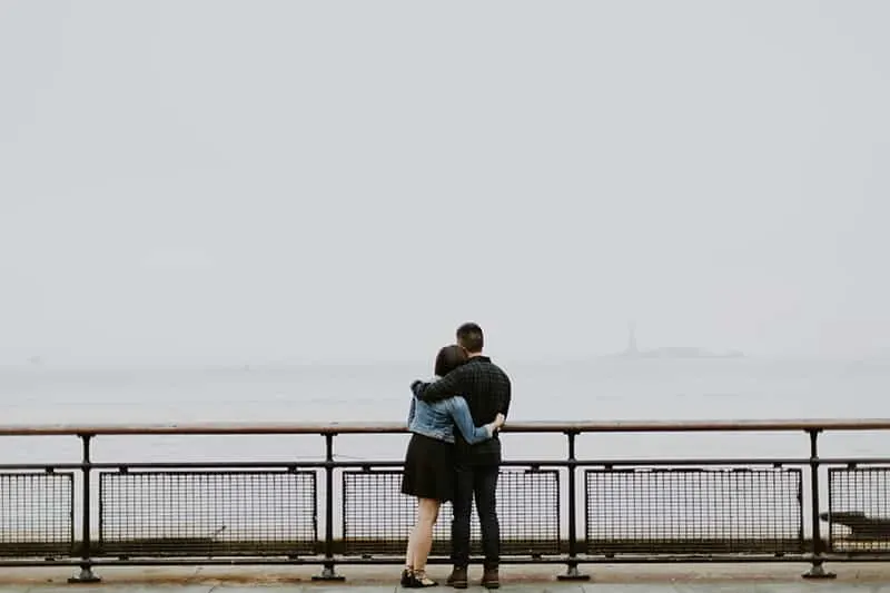 Ein Paar umarmt sich, während es vor einem Zaun in der Nähe des Gewässers steht