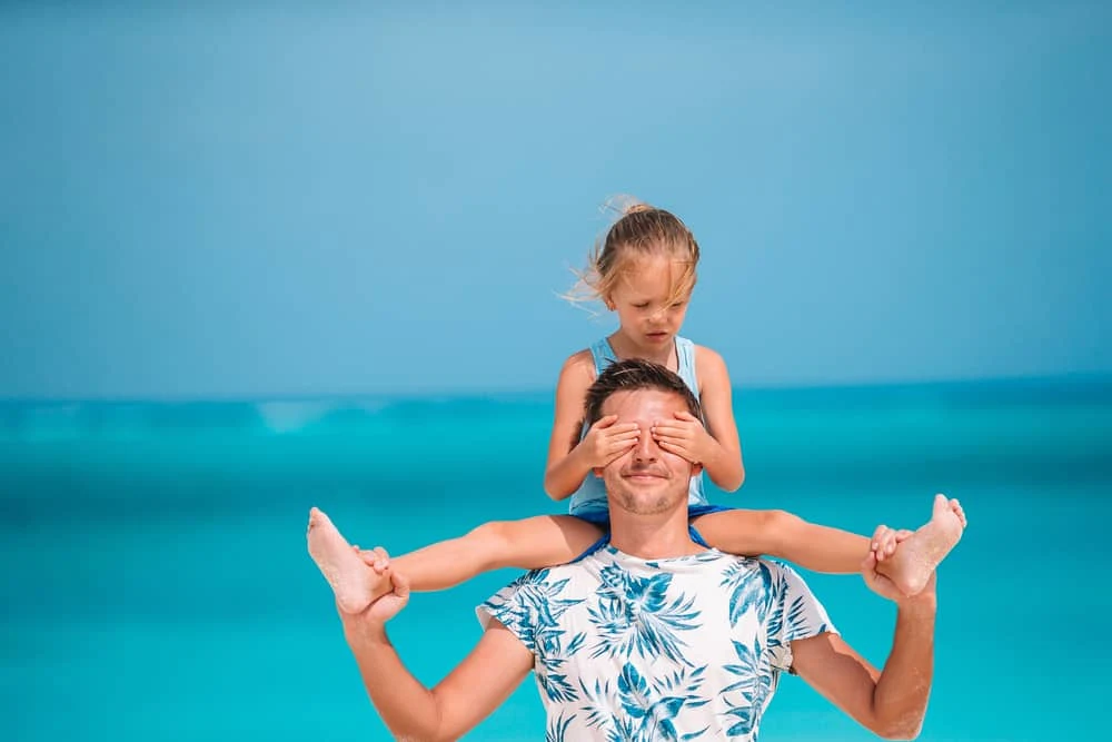Ein Vater am Meer trägt seine Tochter auf den Schultern