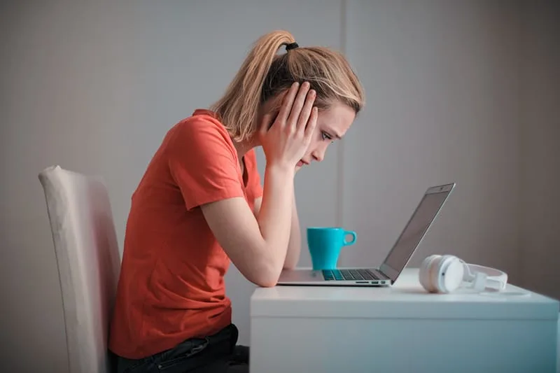 Eine Frau in einem Problem sitzt vor dem Laptop und hält den Kopf
