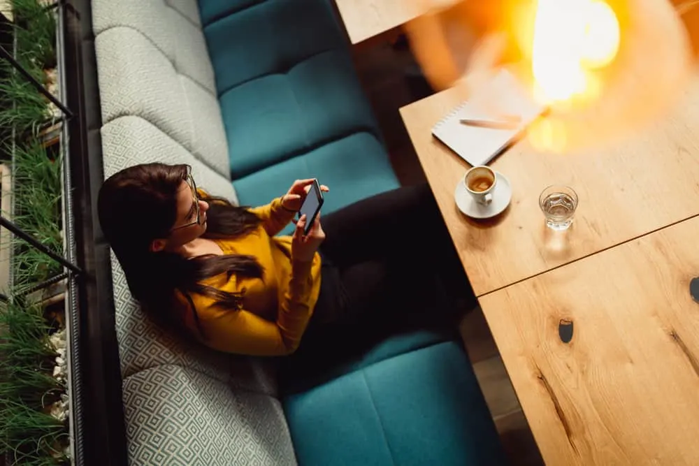 Eine Frau in einem gelben Pullover sitzt in einem Café und benutzt ein Smartphone