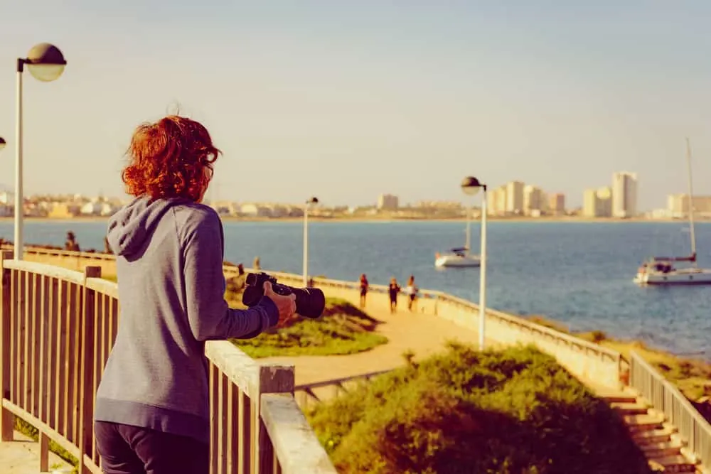 Eine Frau mit einer Kamera steht und beobachtet das Meer