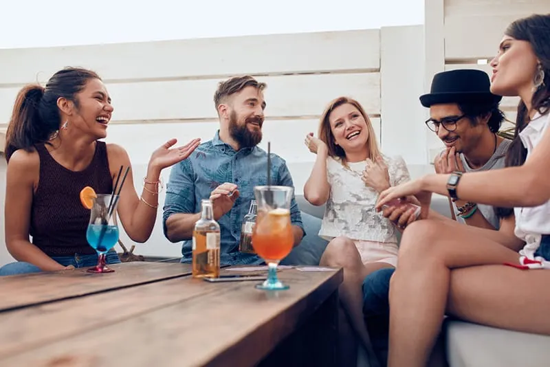 eine Gruppe lachender Freunde, die mit Getränken am Tisch sitzen