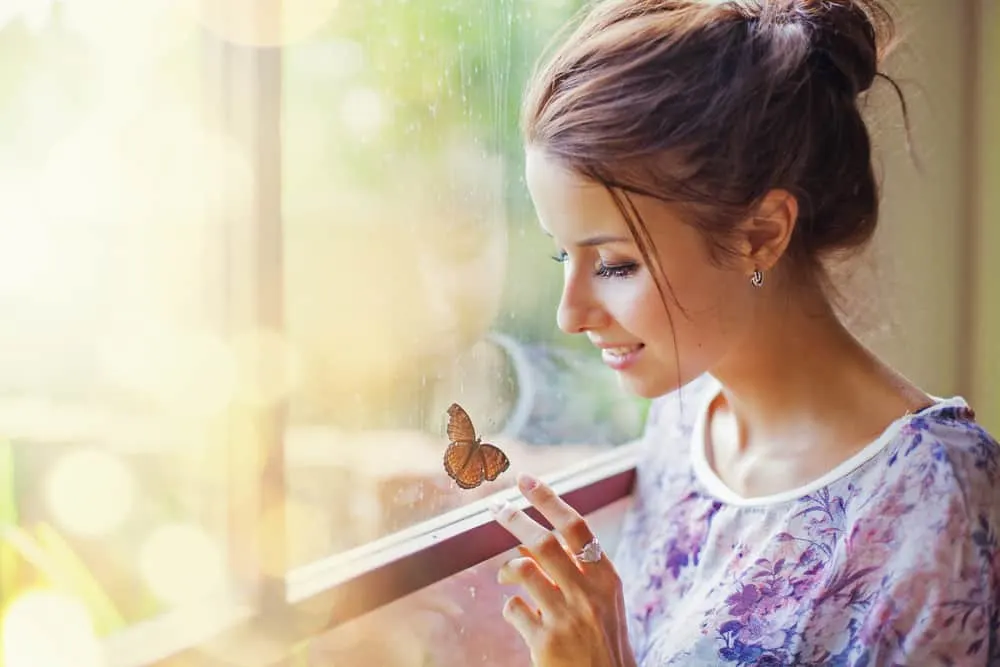 Eine lächelnde Frau am Fenster berührt einen Schmetterling