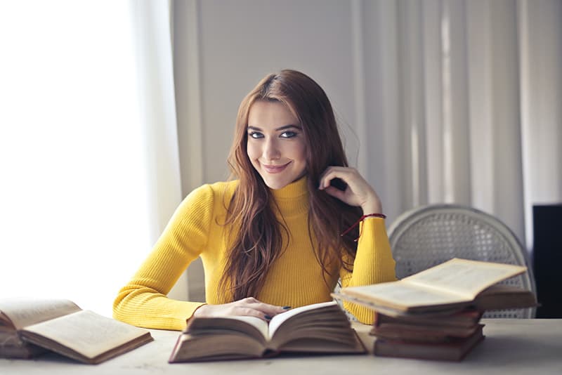 Eine lächelnde Frau, die am Tisch sitzt und ein Buch liest