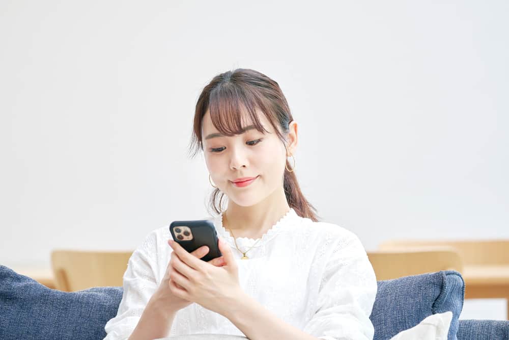 Eine schöne asiatische Frau sitzt auf der Couch und benutzt ein Handy