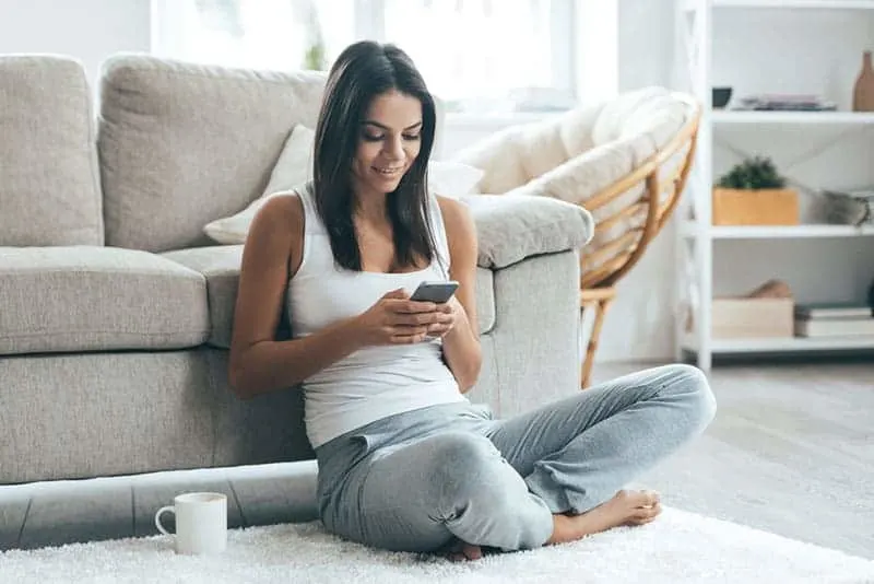 Frau sitzt auf dem Boden und schreibt eine SMS