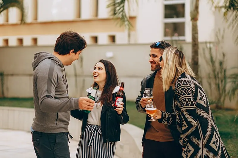 Gruppe lachender Freunde, die ihre Getränke halten, während sie im Hinterhof stehen
