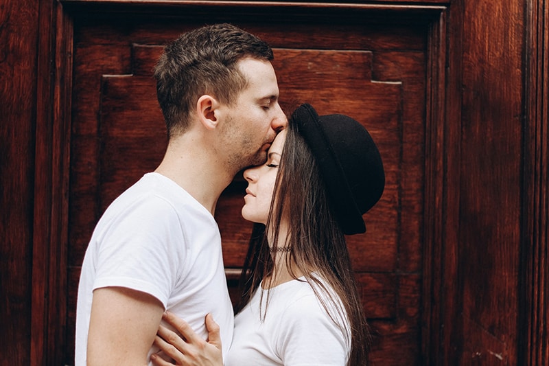 Mann küsste seine Freundin auf die Stirn, während er vor der Tür stand