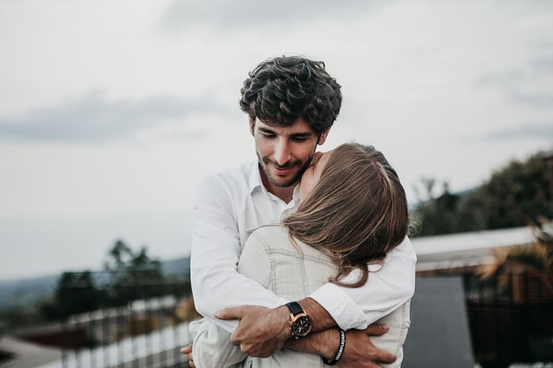 Mann umarmt seine Freundin, während er zusammen auf der Terrasse steht