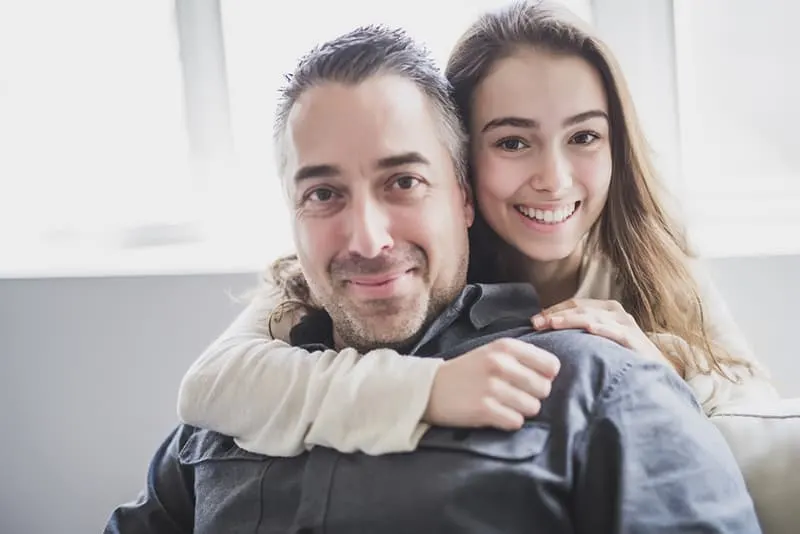 Teenager-Tochter umarmt ihren Vater von hinten im Wohnzimmer