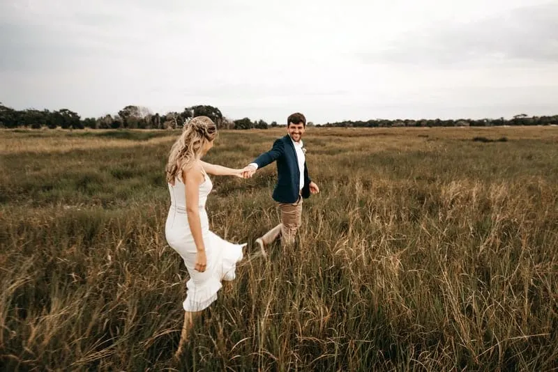 Braut und Bräutigam gehen lächelnd über das Feld