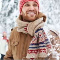 Draußen im Schnee steht ein lächelnder Mann mit einem Schal und einer Wintermütze