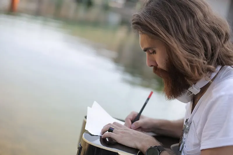 Ein Mann schreibt ein Gedicht auf Papier, während er in der Nähe des Gewässers sitzt