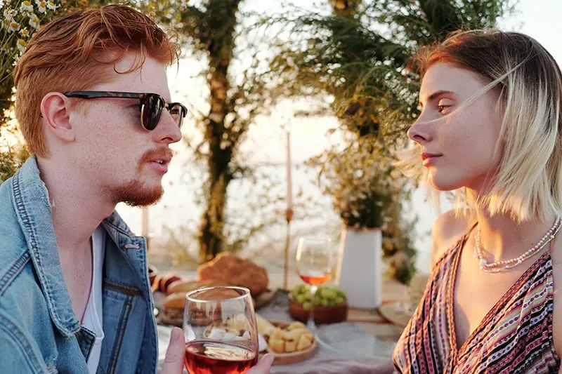 Ein Mann hält ein Glas Wein und spricht mit einer Frau während eines Mittagessens im Freien