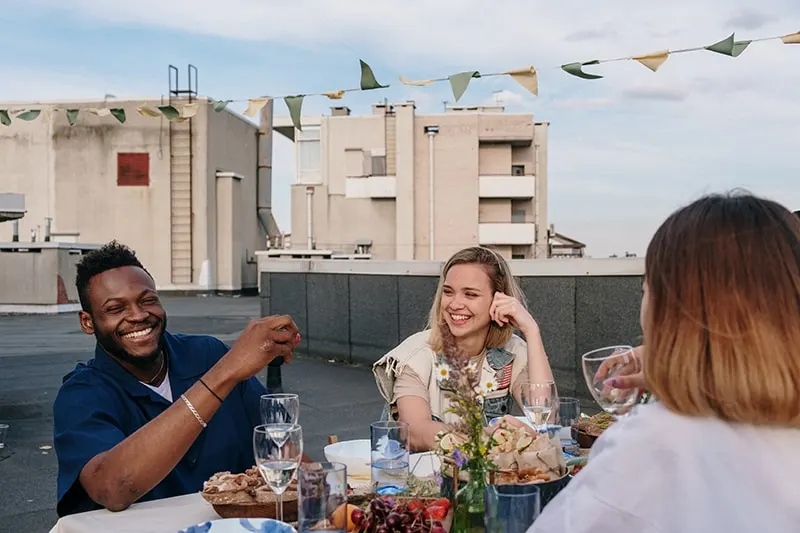 ein lächelnder Mann, der mit Freunden am Tisch auf dem Dach sitzt