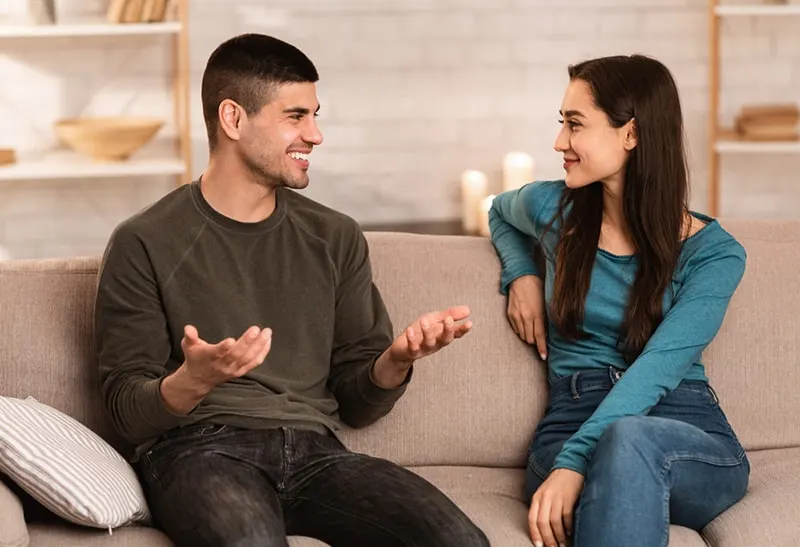 Ein lächelnder Mann und eine lächelnde Frau sprechen, während sie auf der Couch sitzen
