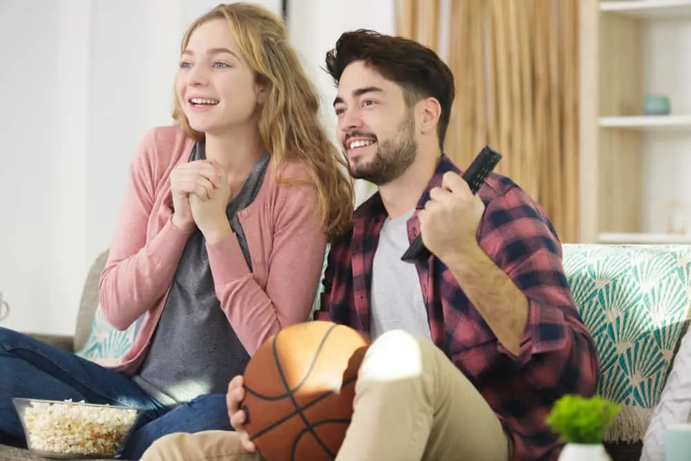 ein lächelndes Liebespaar, das ein Basketballspiel im Fernsehen genau beobachtet